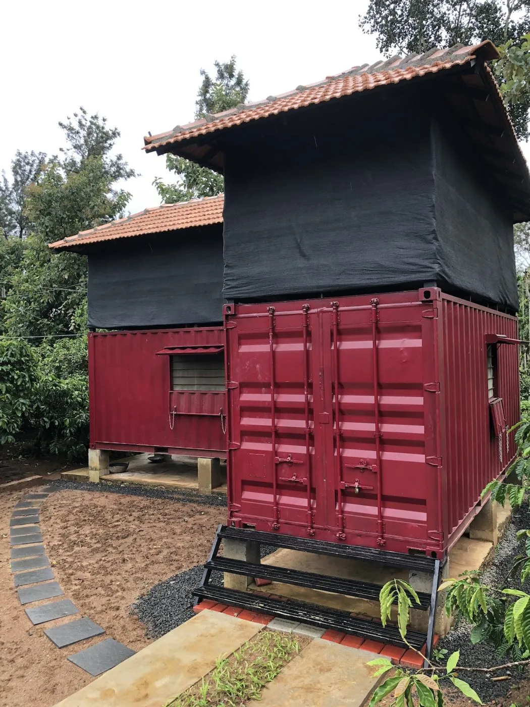 The Steel Box: red shipping containers with the shade-net coworking deck above, surrounded by trees